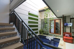 A modern indoor pool area with a staircase, tiled flooring, and a red chair. - Family Villa Sanur (Denpasar)