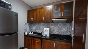 Eine kompakte Küche mit Holzschränken, einem Edelstahlkühlschrank, einer Kaffeemaschine und einer strukturierten Spritzschutzwand.