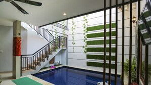 Ein Poolbereich mit Treppe, Wanddekorationen in Grün und einem Deckenventilator.