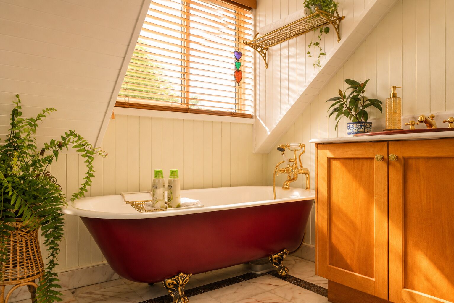 A bathroom with a freestanding bathtub, wooden cabinetry, and a window with blinds.
