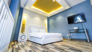 A modern bedroom with a bed, a TV, a console table, and a unique ceiling design.