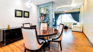 A modern dining area with a round table and upholstered chairs, a decorative wall piece, and a sofa in the background.