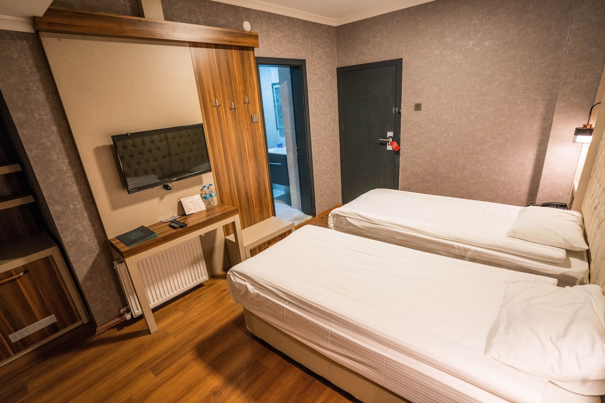 A hotel room with two single beds, a wooden wardrobe, a television, and a desk with a chair.