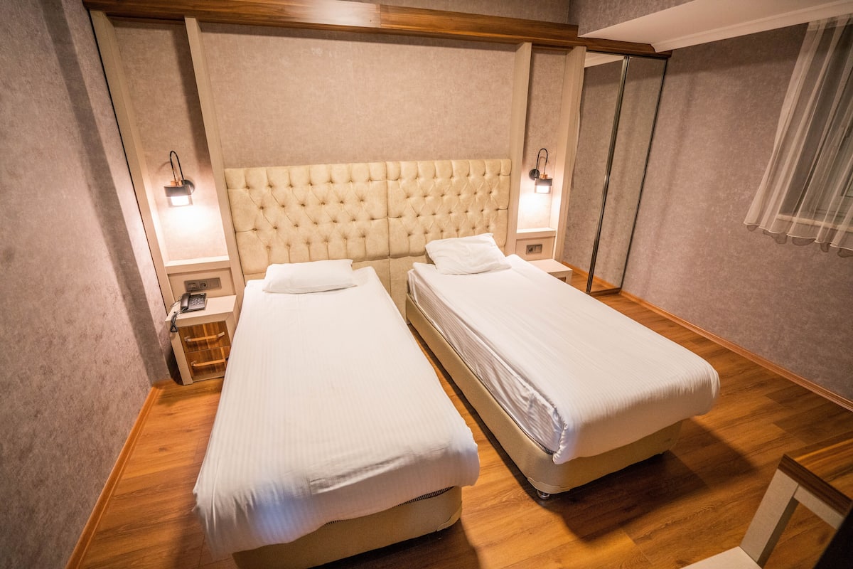 A hotel room with two beds, wooden flooring, and a tufted headboard.