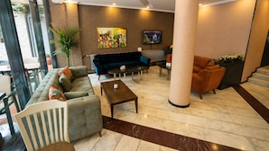 A lobby with a sofa, armchairs, a coffee table, a TV, and a large plant. - Bloom Hotel (Ankara)