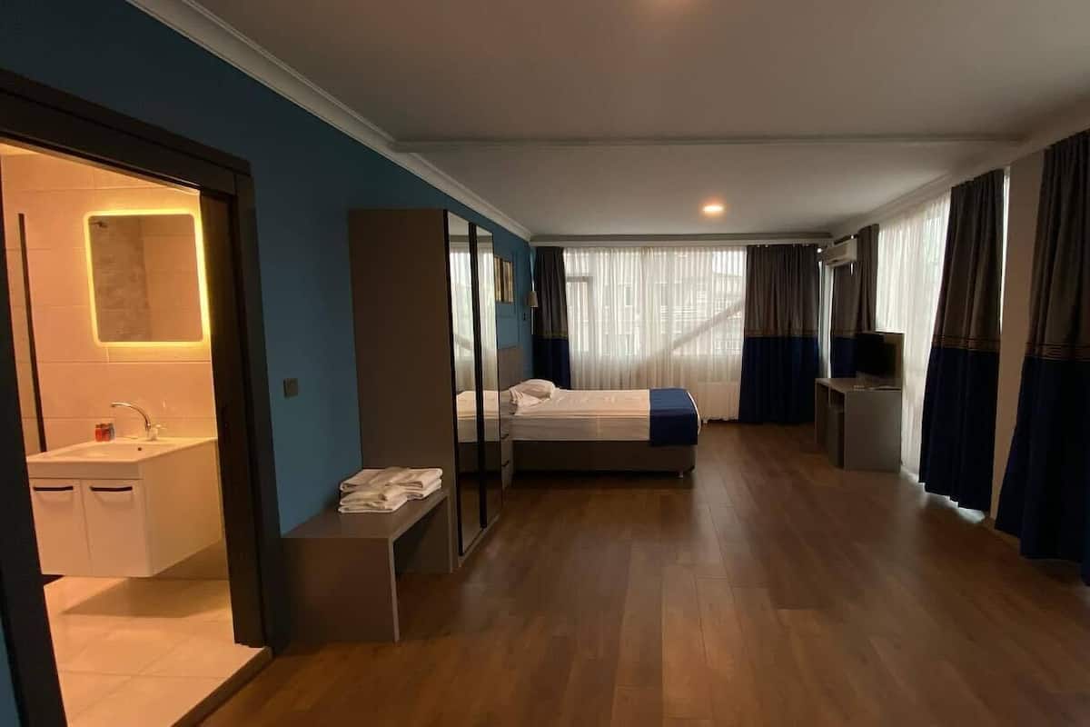 A hotel room with a bed, a bedside table, a desk, a chair, a mirror, a window with curtains, and a bathroom with a sink and mirror.