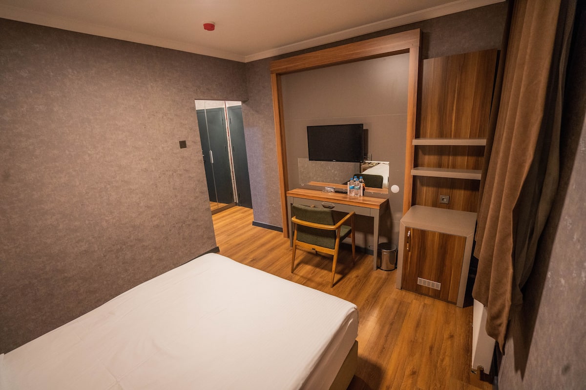 A hotel room with a bed, a desk with a chair, a TV, and a wardrobe.