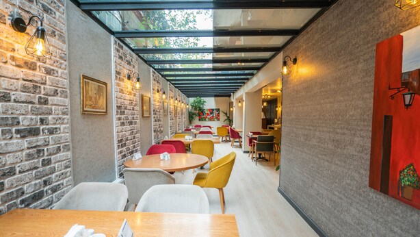 A modern cafe with brick walls, wooden tables, and yellow chairs. - Bloom Hotel (Ankara)
