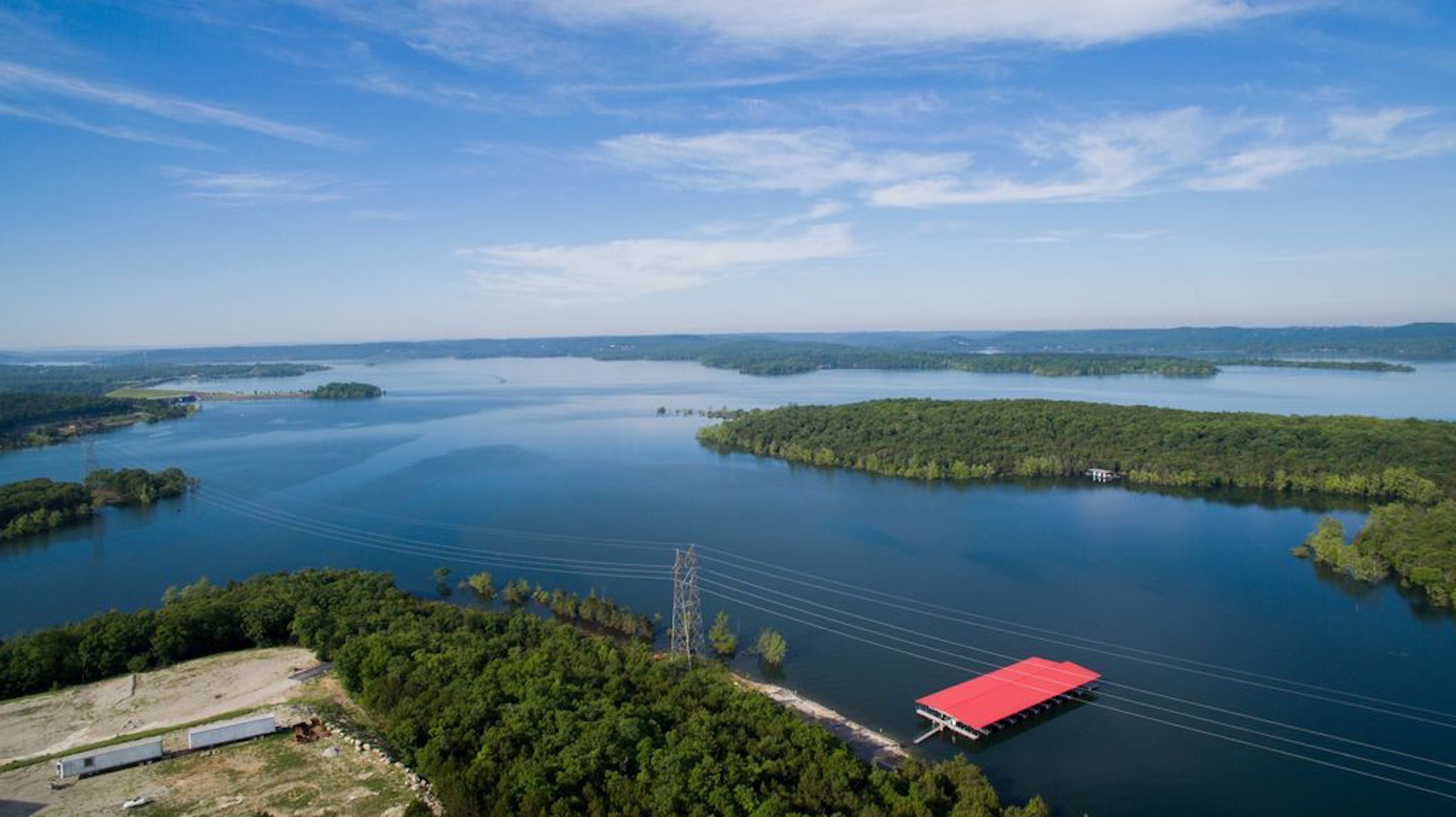 Vista aèria d'un llac envoltat de zones boscoses, amb un moll i una construcció amb teulada vermella.