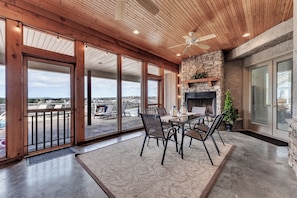 Une vaste terrasse dotée d’une cheminée en pierre, d’un plafond en bois et de grandes portes-fenêtres coulissantes offrant une vue sur le paysage.