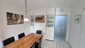 Ein Essbereich mit Holztisch und Stühlen, einer Pendelleuchte sowie zwei an Wänden befestigten Schränken mit Glastüren.