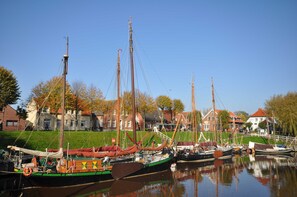 A harbor with several traditional sailing boats docked, surrounded by buildings with red roofs and a grassy area. - No. 97 - Holiday home Uferstraße (Wittmund)