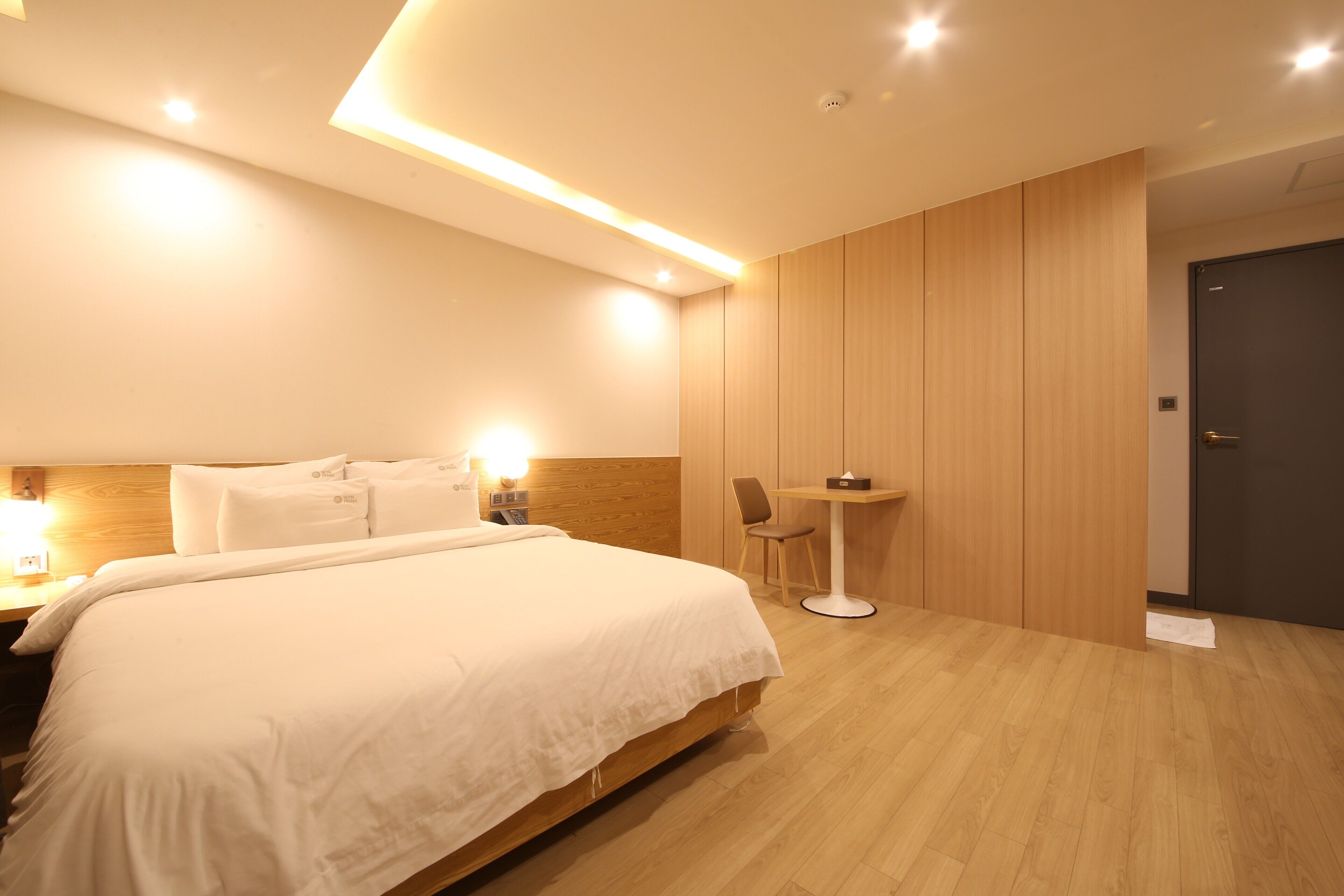 Ein modernes Hotelzimmer mit einem großen Bett, Nachttischen, einem kleinen Tisch mit Stühlen und einer Tür.