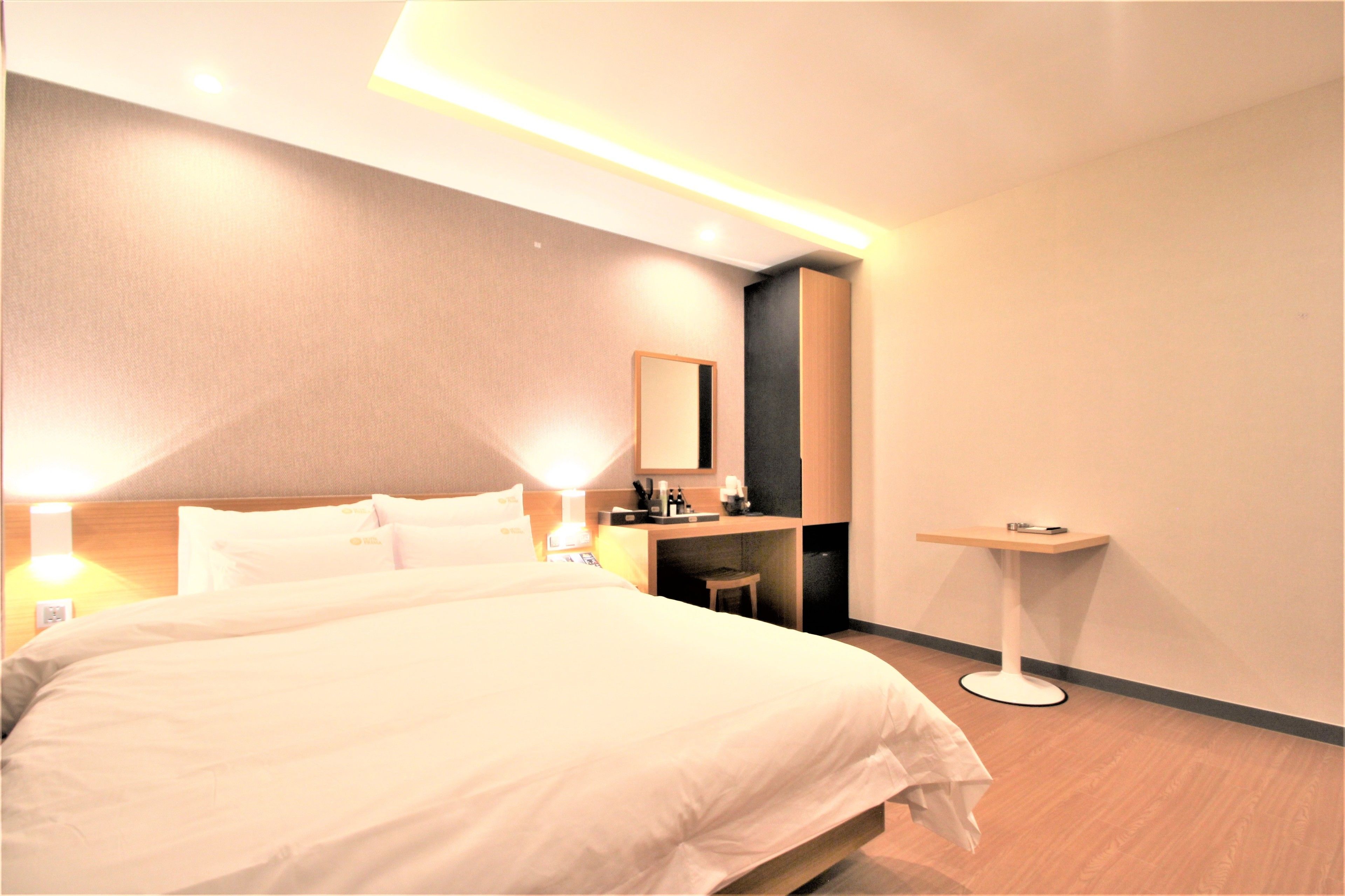 A modern hotel room with a large bed, bedside lamps, a small desk, and a mirror.