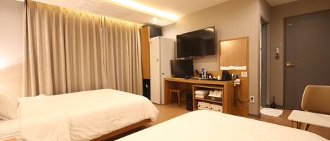 Une chambre d’hôtel avec deux lits, un bureau avec une télévision, un minibar et une porte.