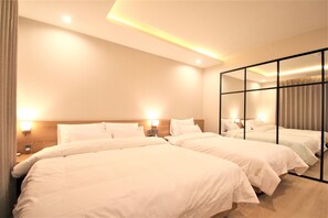 A hotel room with three beds, a large mirror, and wall-mounted lights.