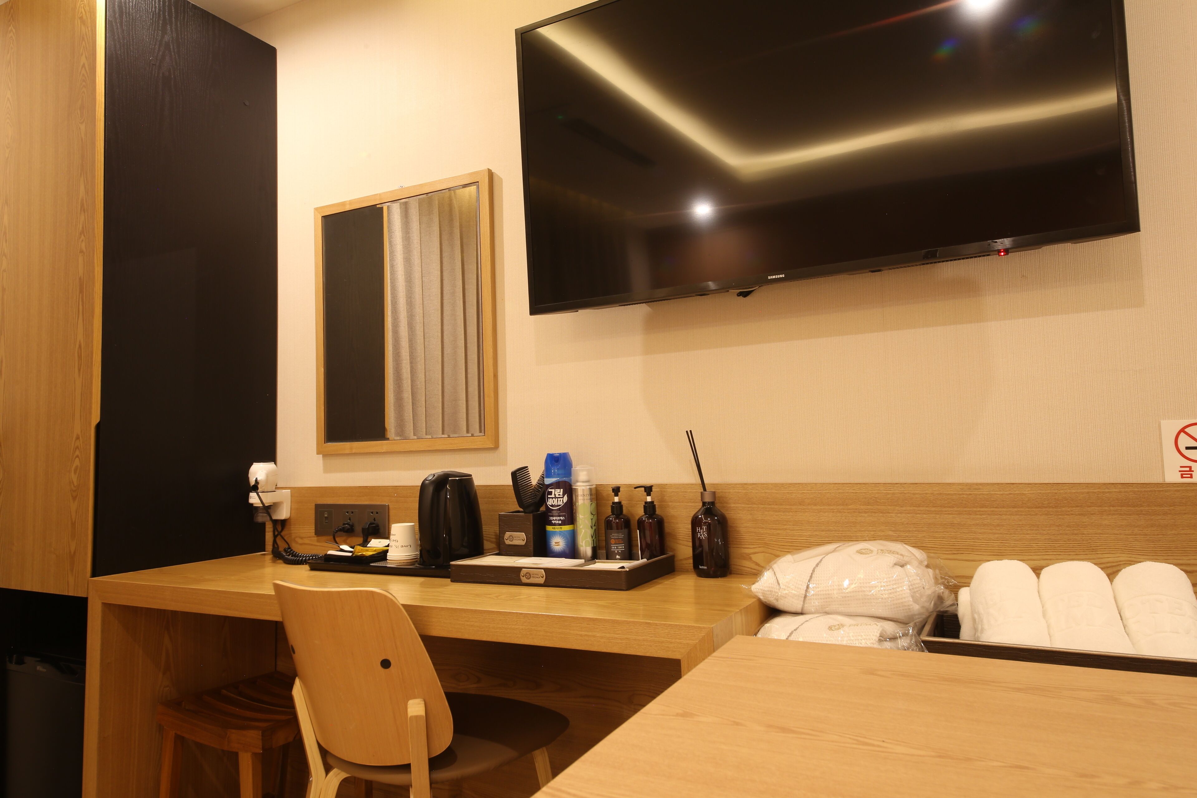A hotel room with a wooden desk, a flat-screen TV, a mirror, and toiletries.