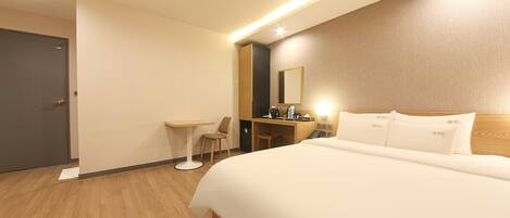 A hotel room with a large bed, a desk, a chair, and a mirror.