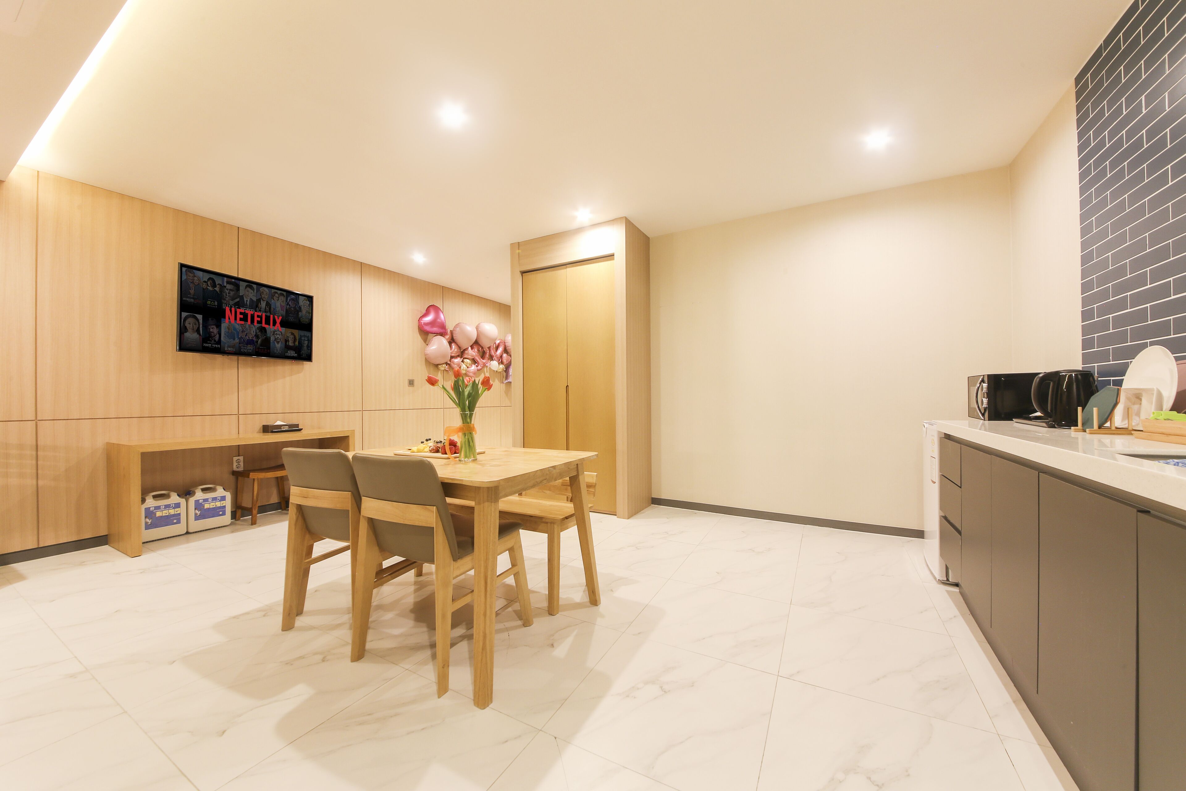 Cocina moderna con una mesa de comedor de madera, sillas y un televisor en la pared mostrando el logotipo de Netflix.