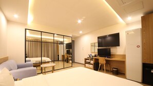 A hotel room with a large bed, a desk with a chair, a television, and a wardrobe. - Hotel Prima (Busan)