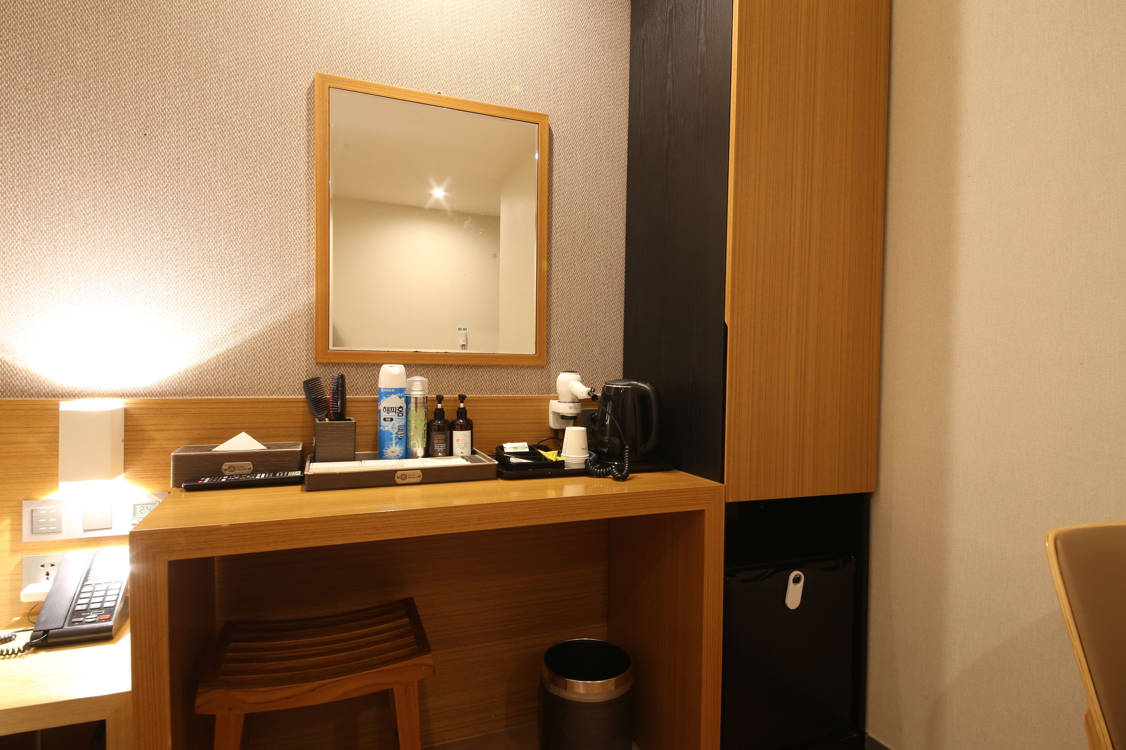 A hotel room with a wooden desk, a mirror, a telephone, a coffee maker, and a trash can.