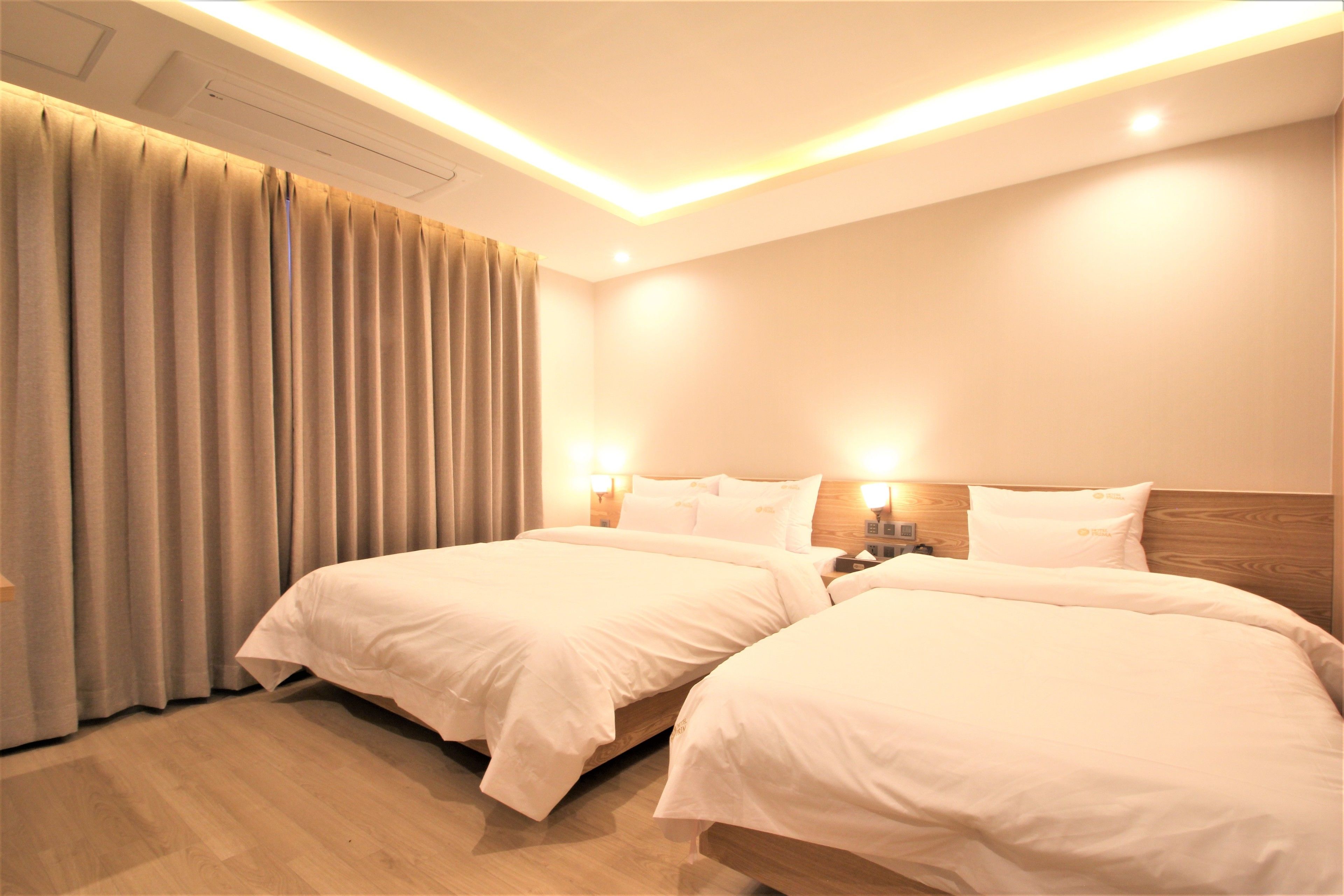 A hotel room with two beds, a wooden headboard, and a ceiling light fixture.