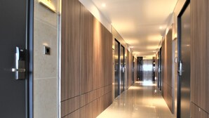 A modern hallway with a polished floor, wooden paneling on the walls, and a series of doors. - Hotel Prima (Busan)