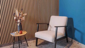 Une chaise avec un coussin et une structure en métal, une petite table ronde ornée d’un vase contenant des plantes séchées et un magazine.