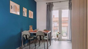 Un coin repas avec une table et des chaises, un mur bleu orné de tableaux encadrés et une vue à travers une porte vitrée.