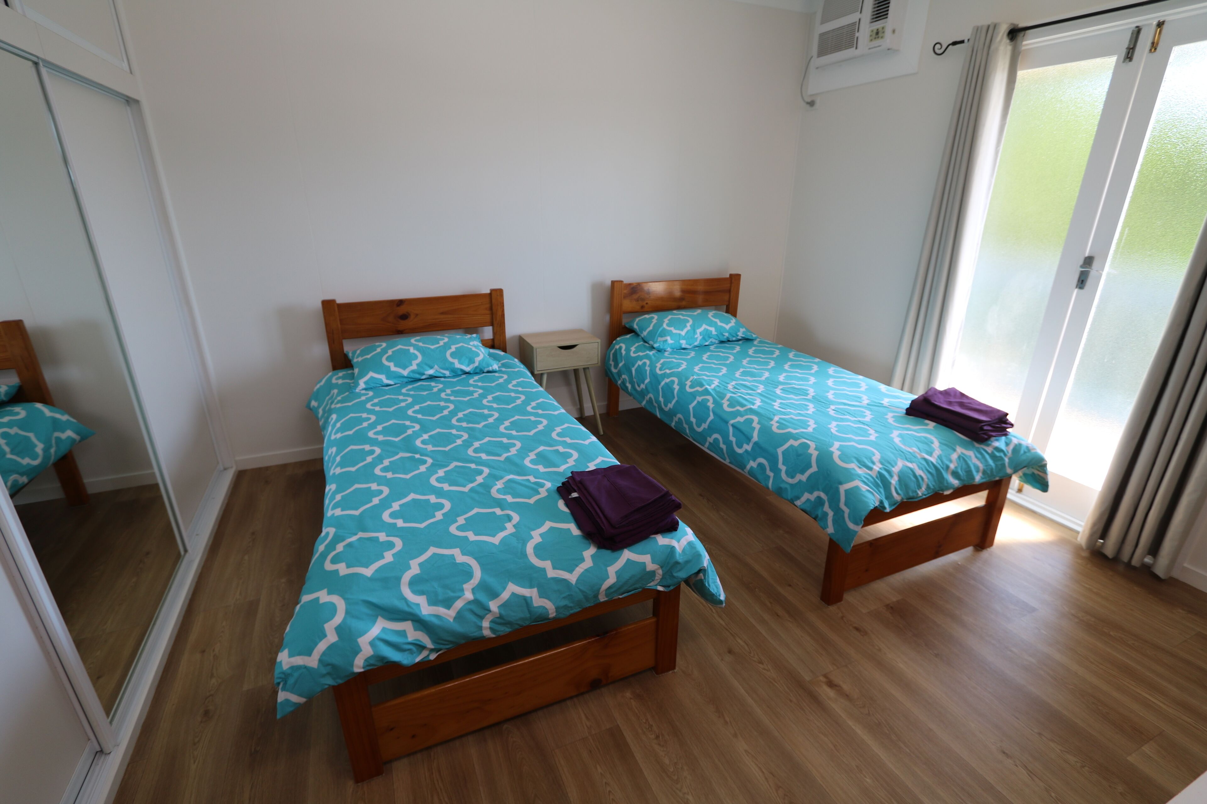 A room with two wooden beds, each with a patterned blue and white bedspread and a purple towel on one bed.