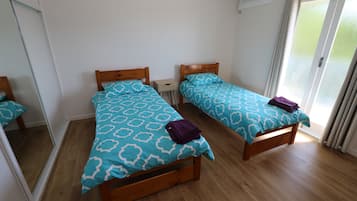A room with two wooden beds, each with a patterned blue and white bedspread and a purple towel on one bed.