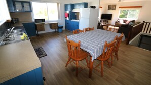 A compact kitchen with blue cabinets, a dining table with chairs, and a small seating area with a sofa and TV.