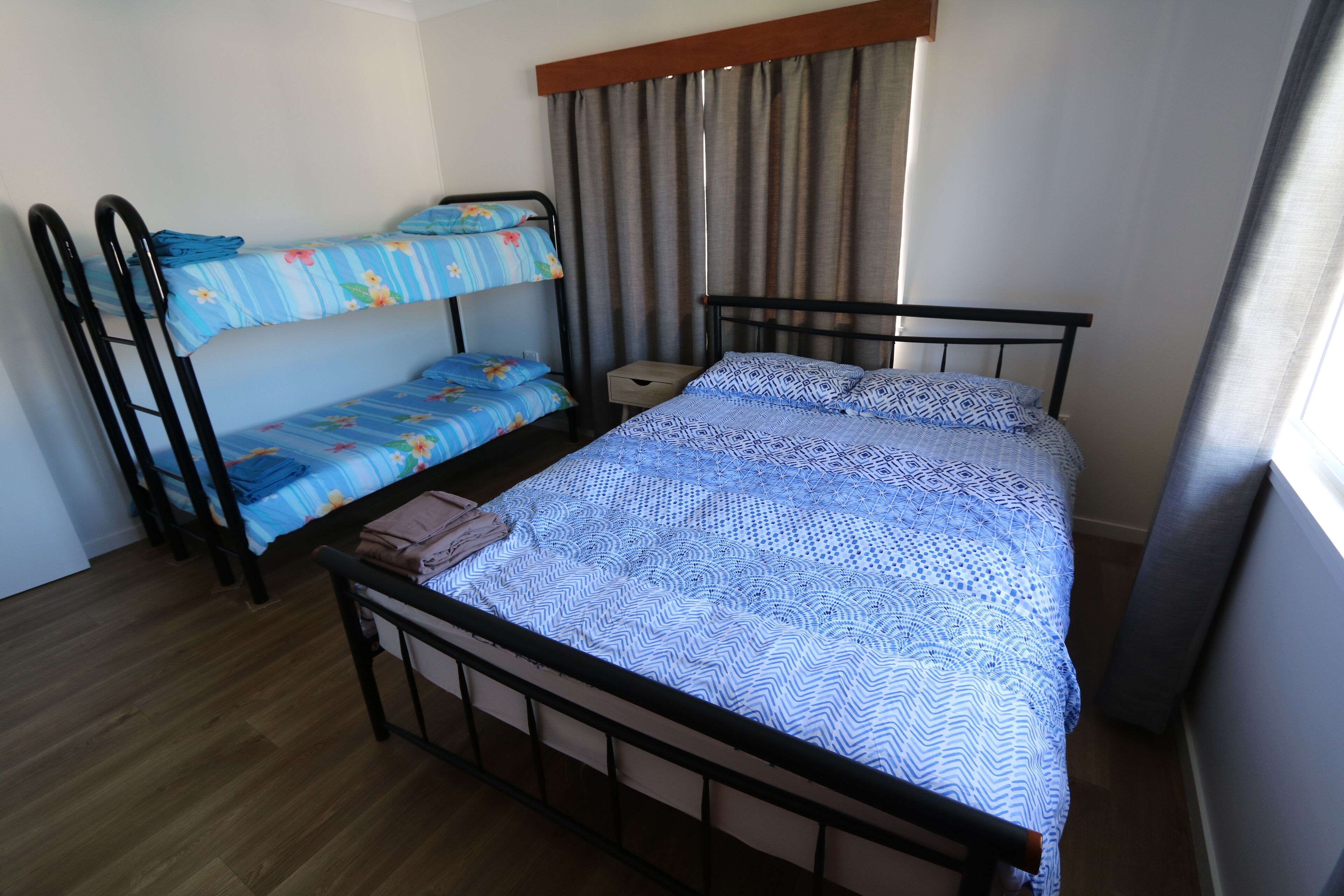 Une chambre avec un lit superposé, un lit simple, une table de chevet et une fenêtre avec des rideaux.