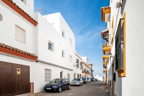 A narrow street lined with white buildings, parked cars, and a clear blue sky.