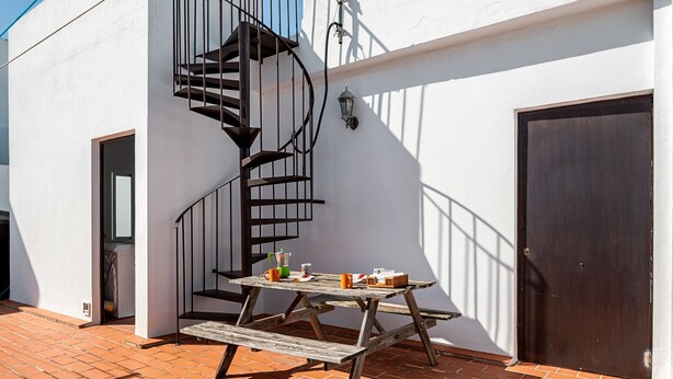 Um pátio com mesa e bancos de madeira, uma escada em caracol e uma porta.
