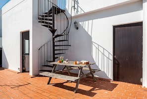 A patio with a wooden table and benches, a spiral staircase, and a door.