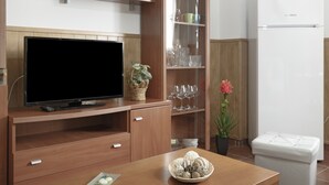 Cozinha moderna com televisão de tela plana, armários de madeira, geladeira branca e uma mesa de jantar com um objeto decorativo.