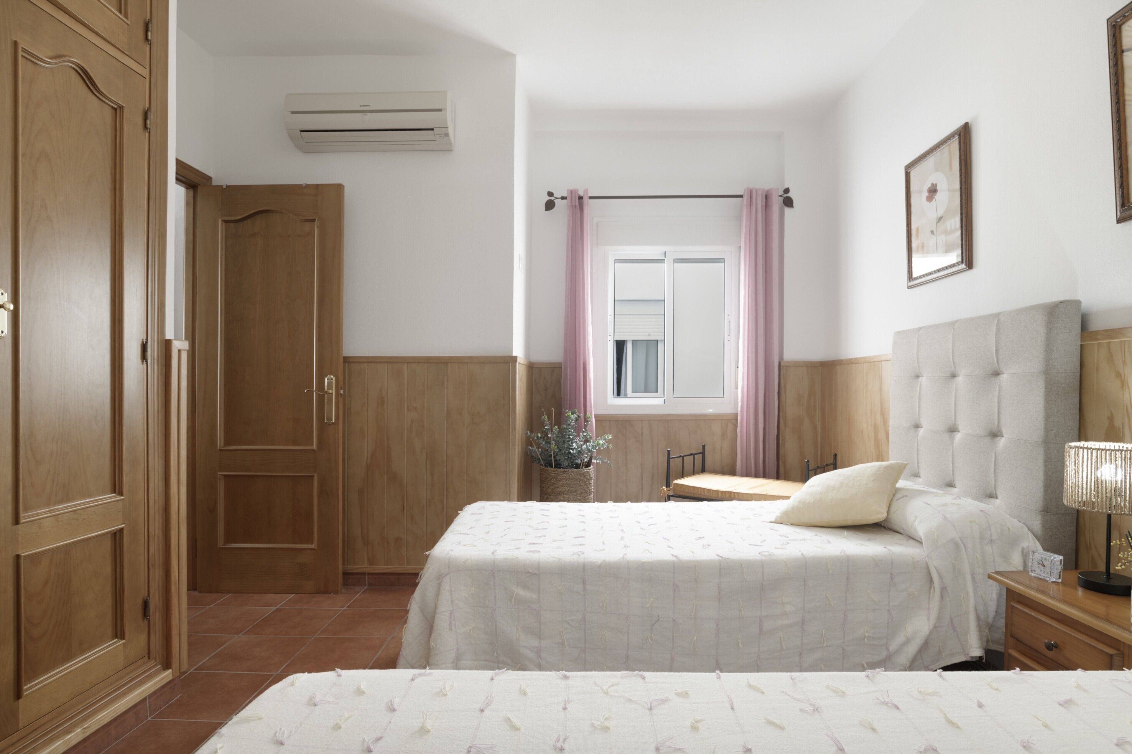 Une chambre à coucher avec un lit, une table de chevet, une lampe et une fenêtre avec des rideaux.