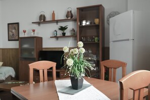 A dining area with a table, chairs, a vase with flowers, a television, and shelves with various items.