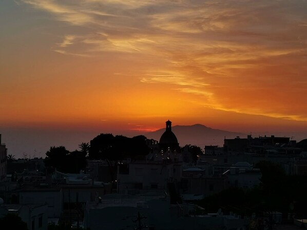 Um pôr do sol sobre uma paisagem urbana, com uma estrutura em cúpula proeminente silhuetada no céu.