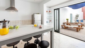 A modern kitchen with a stainless steel range hood, a refrigerator, and a dining area with a wooden table and benches. - Cozy town house with private swimming pool (Pollença)