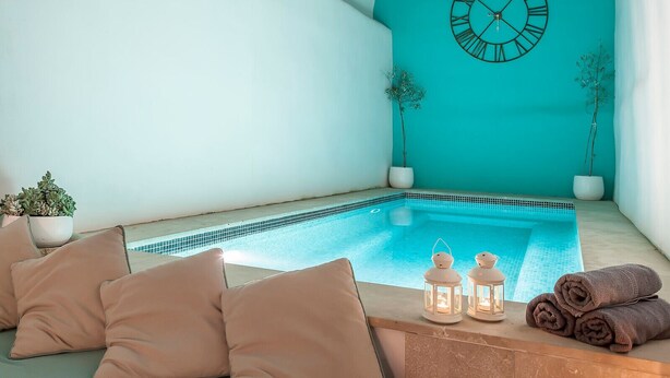 A turquoise room with a pool, a clock, and a sofa with cushions. - Cozy town house with private swimming pool (Pollença)
