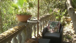 A patio with a stone balustrade, a wicker chair with a cushion, a small table, and a potted plant. - Separate air-conditioned bedroom, summer kitchen with steps and swimming pool (Sartène)