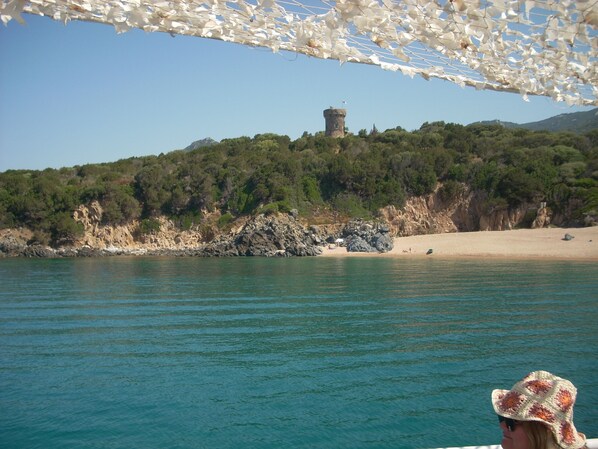 A coastal landscape with a tower on a hill, calm water, and a beach. - Separate air-conditioned bedroom, summer kitchen with steps and swimming pool (Sartène)