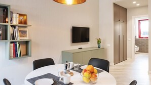 A modern dining area with a round table, chairs, a bowl of fruit, a coffee pot, and a bookshelf with books. - GuestHost - Delightful one bedroom apartment particularly welcoming, with attention to detail and very bright. It has all the necessary comforts.Located in front of the Maggiore hospital, you can easily reach the historic center, the station, the airport (Bologna)