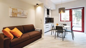 A modern living room with a sofa, dining table, chairs, and a kitchen area. - GuestHost - Delightful one bedroom apartment particularly welcoming, with attention to detail and very bright. It has all the necessary comforts.Located in front of the Maggiore hospital, you can easily reach the historic center, the station, the airport (Bologna)