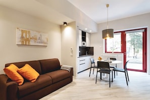A modern living room with a sofa, dining table, chairs, and a kitchen area.