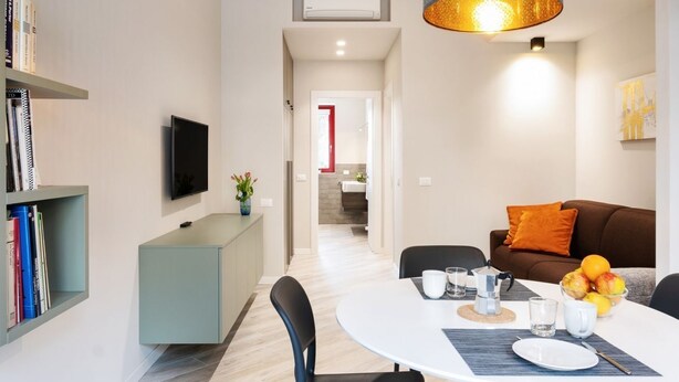 A modern living room with a dining table, a sofa, a TV, and a bookshelf. - GuestHost - Delightful one bedroom apartment particularly welcoming, with attention to detail and very bright. It has all the necessary comforts.Located in front of the Maggiore hospital, you can easily reach the historic center, the station, the airport (Bologna)