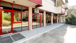 A building with red-framed glass doors, a concrete ground floor, and a white upper section. - GuestHost - Delightful apartment in a strategic position: close to the Ospedale Maggiore, 15 minutes by car from the center and close to public transportation. In the immediateneighborhood you can find restaurants, bars, supermarket and pharmacy.The apar (Bologna)