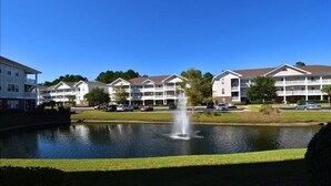 Et hotel med en sø og springvand, omgivet af parkering og grøn bevoksning.